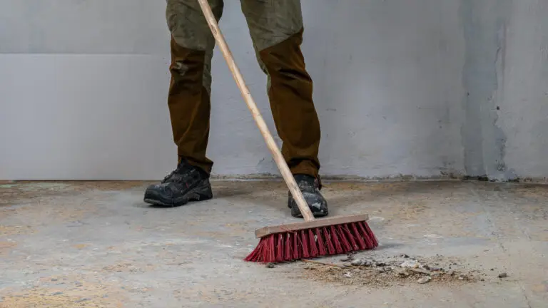 Person sweeping debris on a concrete floor with a red broom.