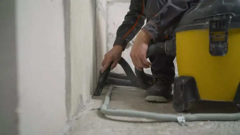 Worker washes the floor with a vacuum cleaner from industrial concrete dust and cement mud during home renovation. A worker vacuums a concrete floor.