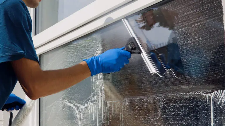 Male professional cleaning service worker in overalls cleans the windows and shop windows of a store with special equipment.